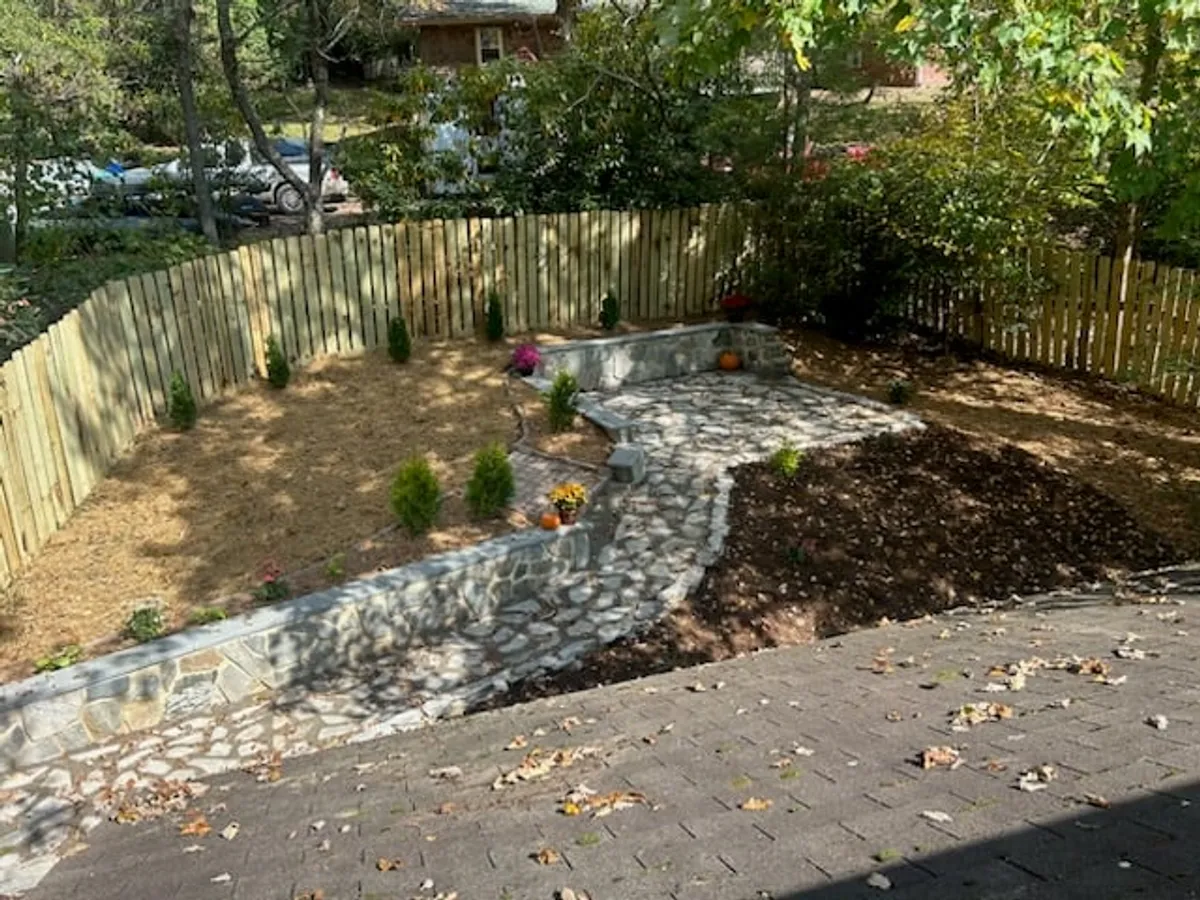 This image features a tranquil backyard with a stone pathway, flower pots, a sturdy fence, and steps leading into the garden area. The space looks welcoming for families, with plenty of room for children to play safely and adults to relax or host outdoor gatherings.