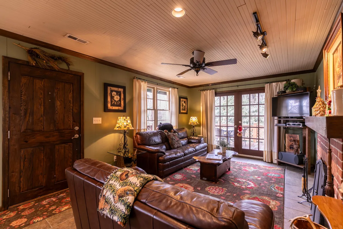 This image captures a warm and welcoming living area with supple leather sofas, a central coffee table, a glowing wood-burning fireplace, large windows bringing in natural light, and decorative lamps that add to the cozy ambiance. The space is clearly curated for relaxation and features upscale yet mountain-inspired furnishings.