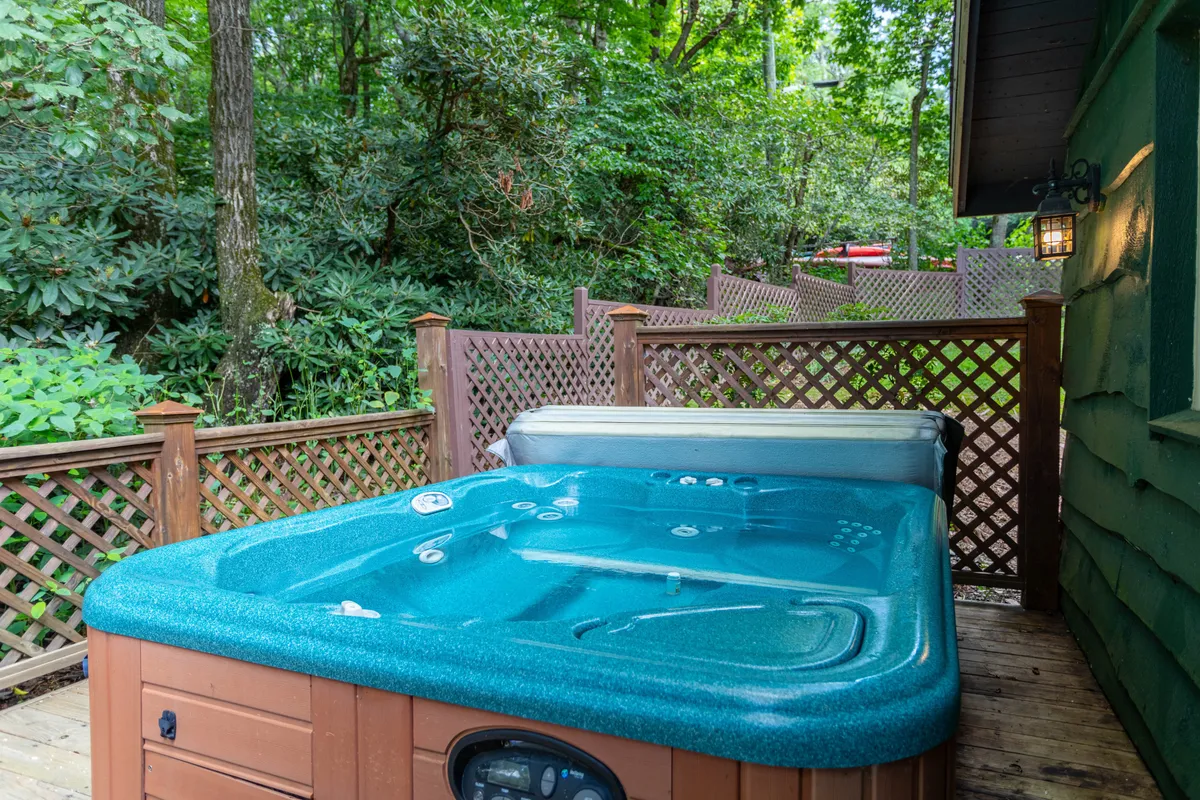 A tranquil corner of the deck showcases the hot tub tucked within lush greenery and enclosed by a fence, emphasizing privacy and immersion in nature. The image evokes relaxation and a true mountain retreat vibe.