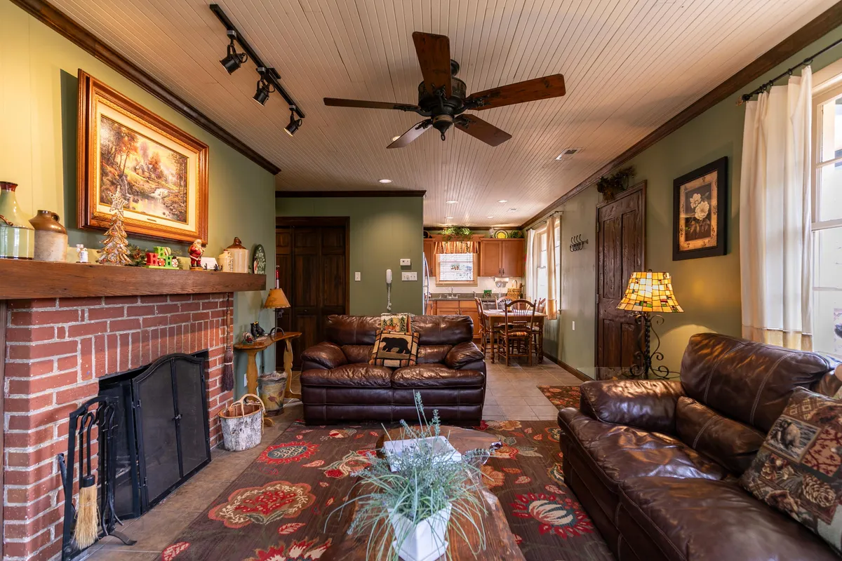 The image shows a designer living space with a prominent stone fireplace, comfortable sofas, curated artwork, and a glimpse of the dining area. The overall mood is cozy, with design elements that reflect both boutique style and cabin character, tying in with the section’s emphasis on artful living.