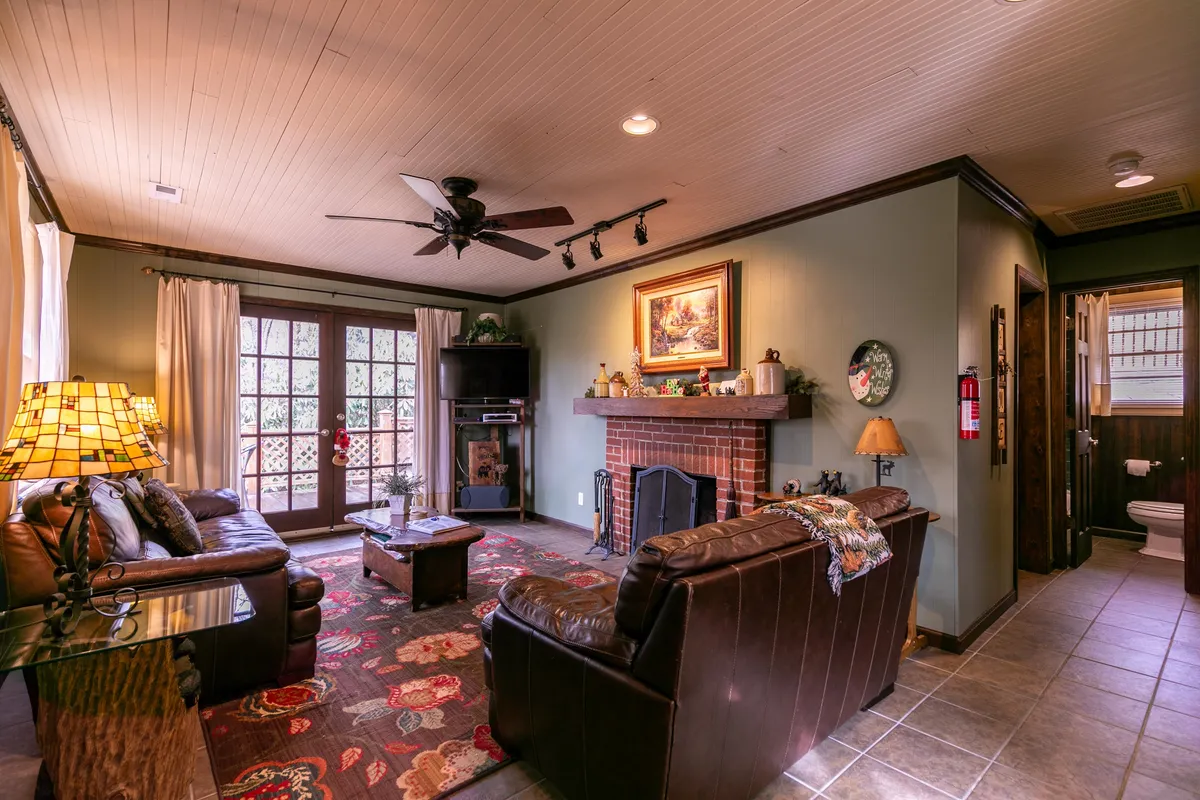 A view of the living area featuring a comfortable sofa, a glowing fireplace, and whimsical artwork above the mantel. The decor hints at playful, artisan touches, and the mood is both inviting and distinctive, echoing the boutique cabin narrative.